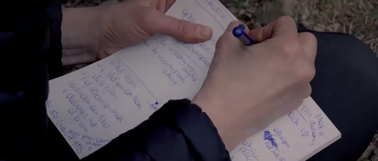 Iemand schrijft met een pen in een notitieboekje, buiten.